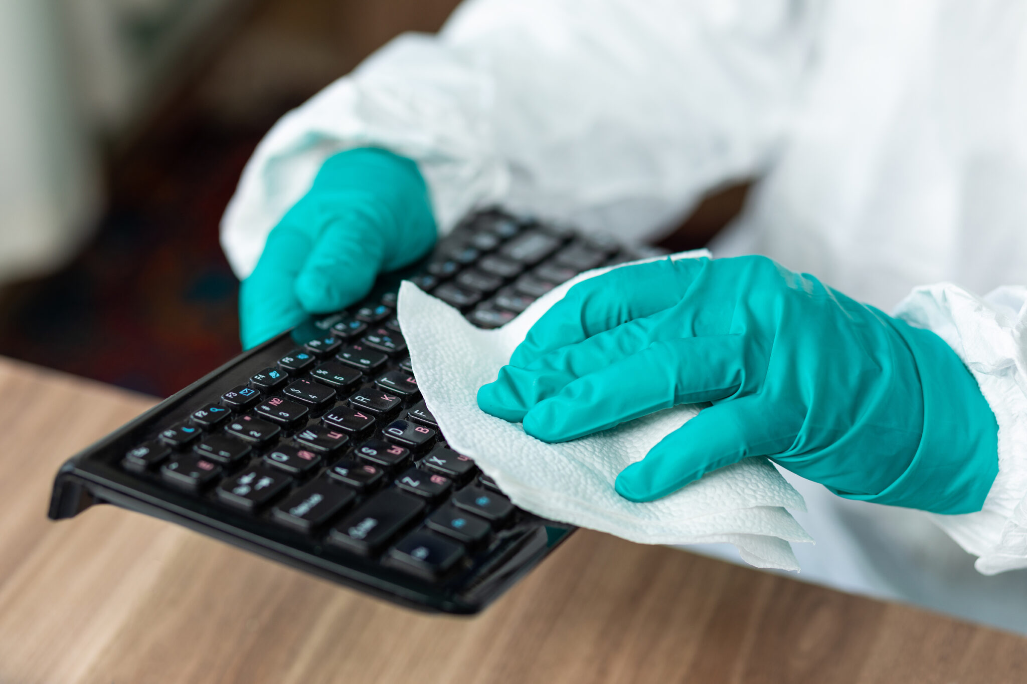 Disinfection man with special white suite cleaning a PC computer keyboard